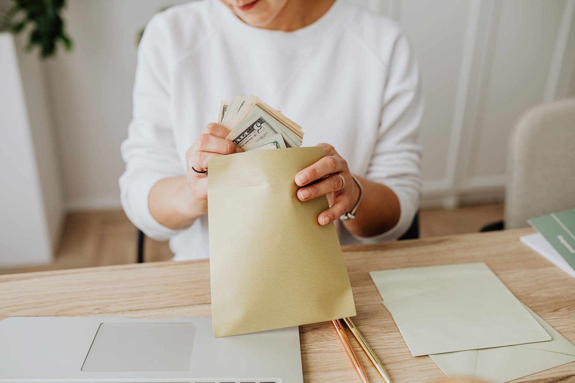 A person holding envelopes with cash at a wooden desk