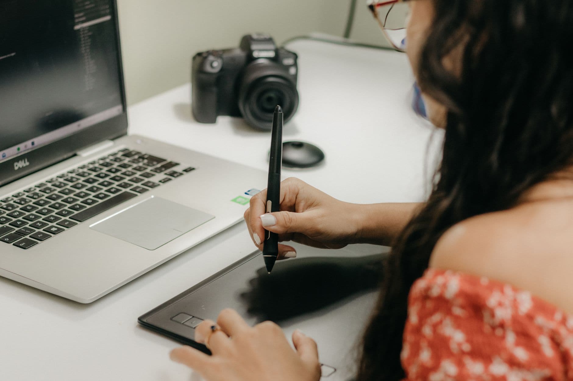 A woman using a digital tablet and stylus next to a laptop