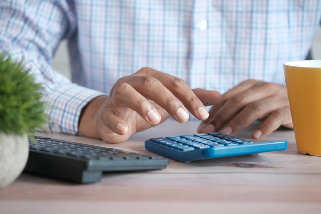 A person using a calculator at a desk with a coffee mug