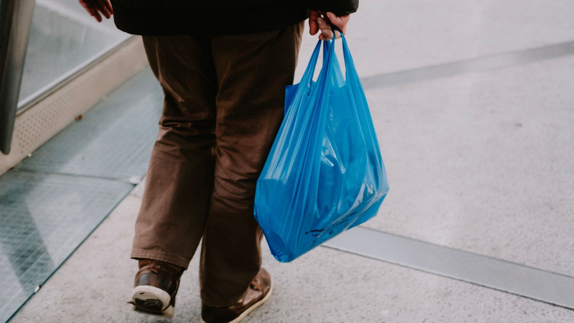 A man carrying groceries in a plastic bag on a sidewalk