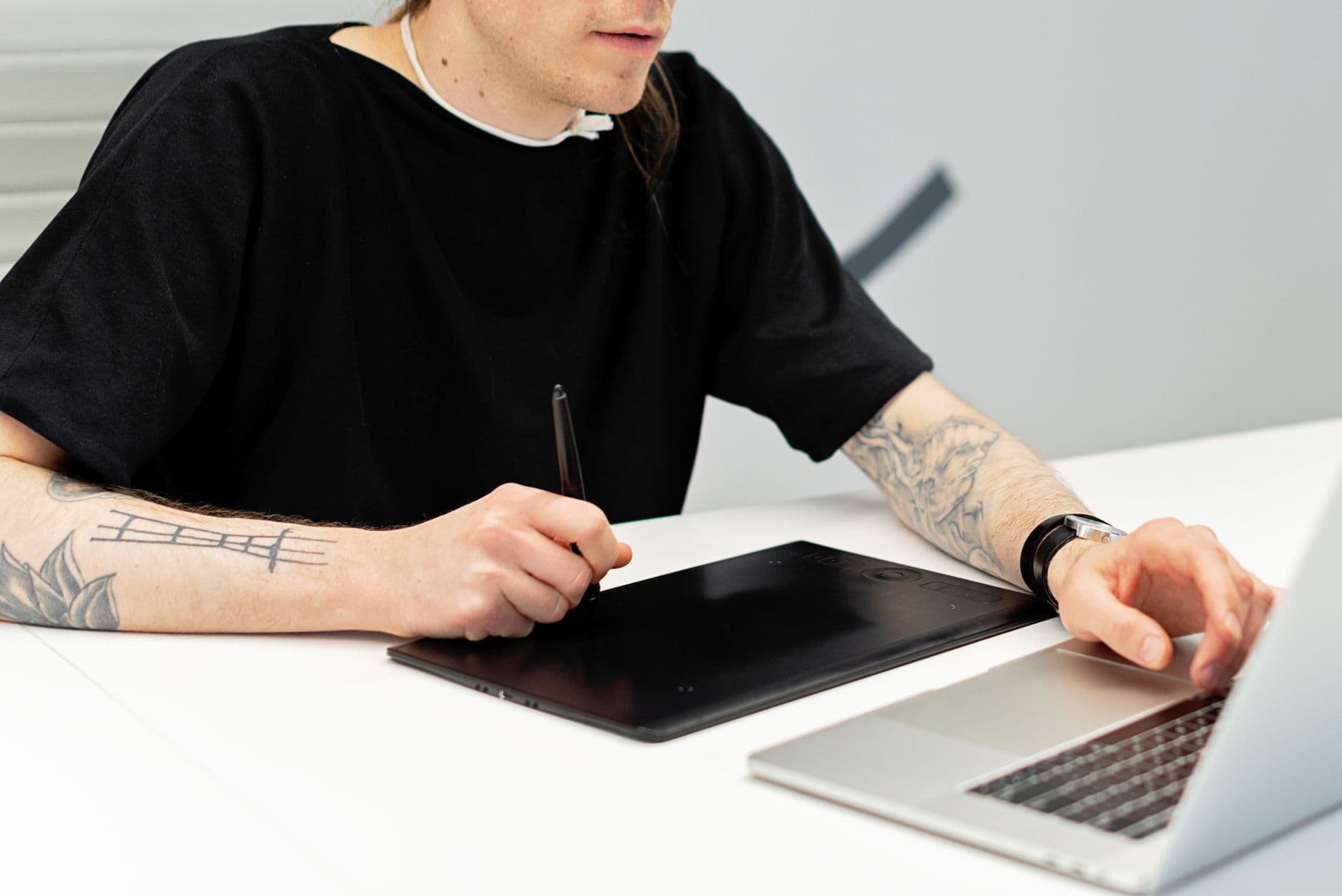 An artist working on a graphics tablet next to a laptop