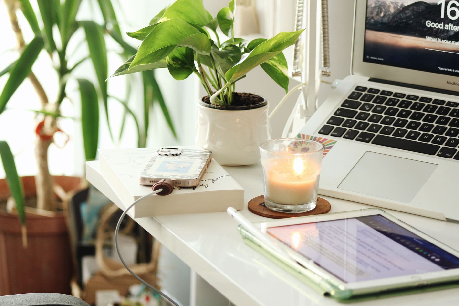 A peaceful home office desk with a laptop, a candle and plants