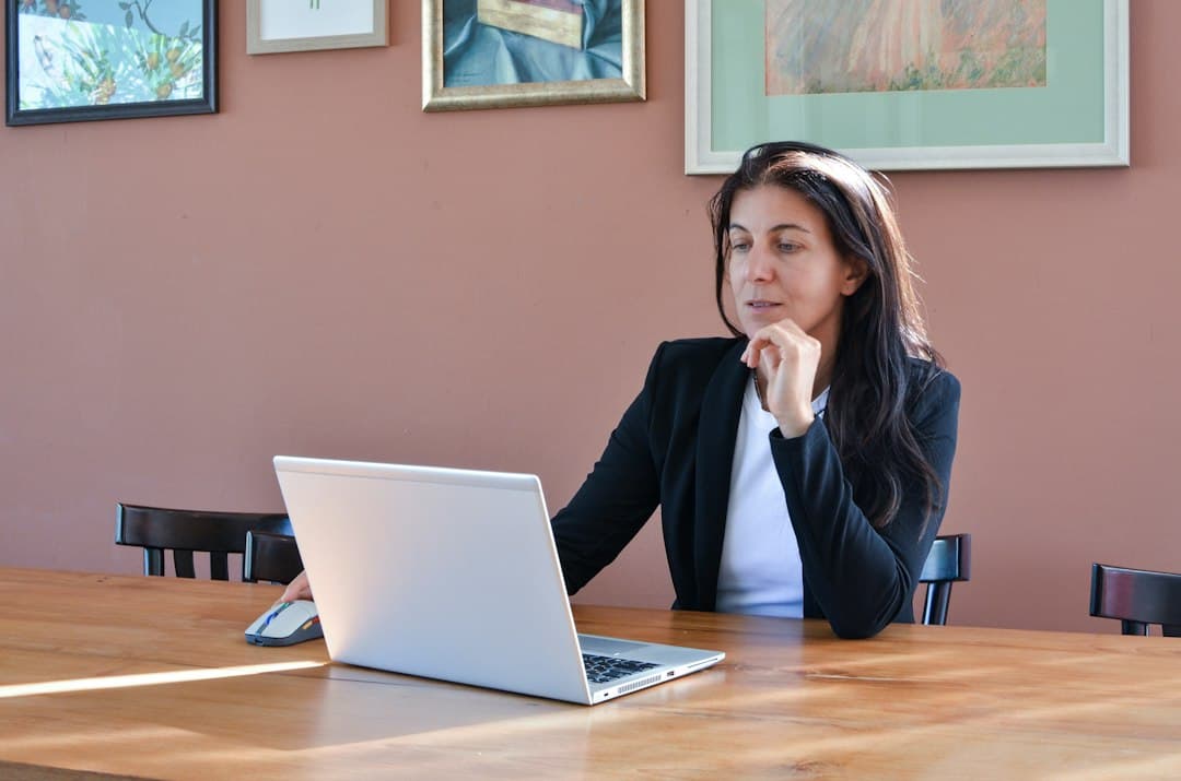 A woman in a black blazer working on a laptop