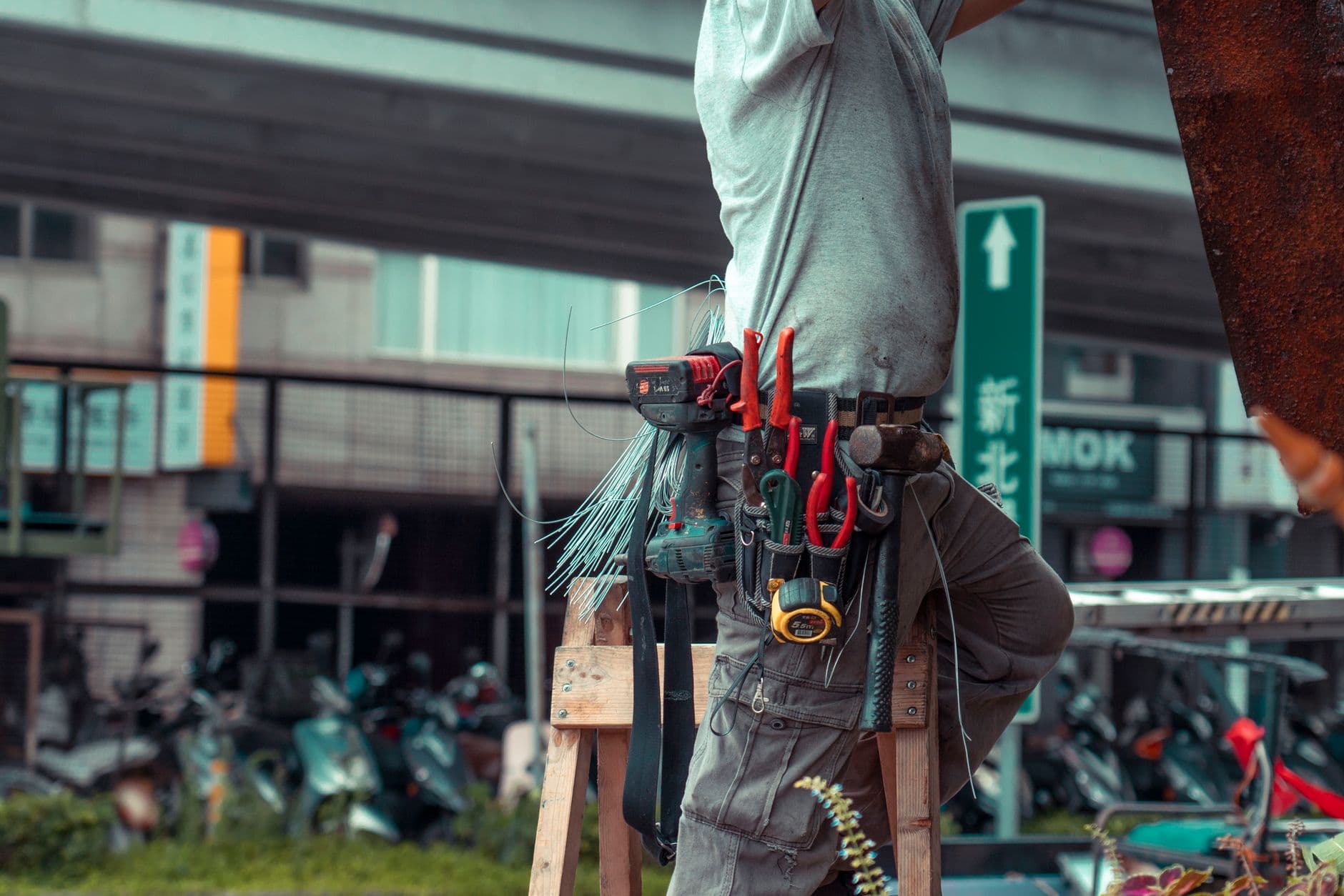 A handyman on a ladder with a tool belt repairing a house