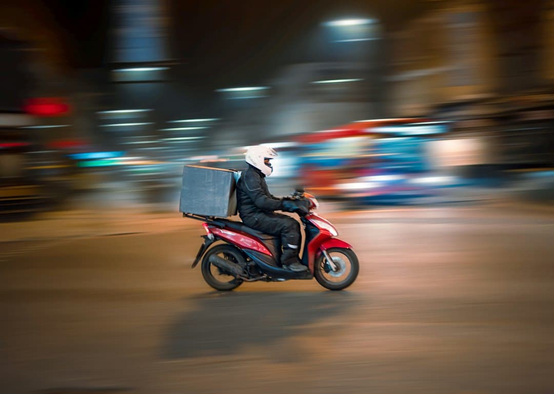 A delivery driver on a scooter riding through a city at night