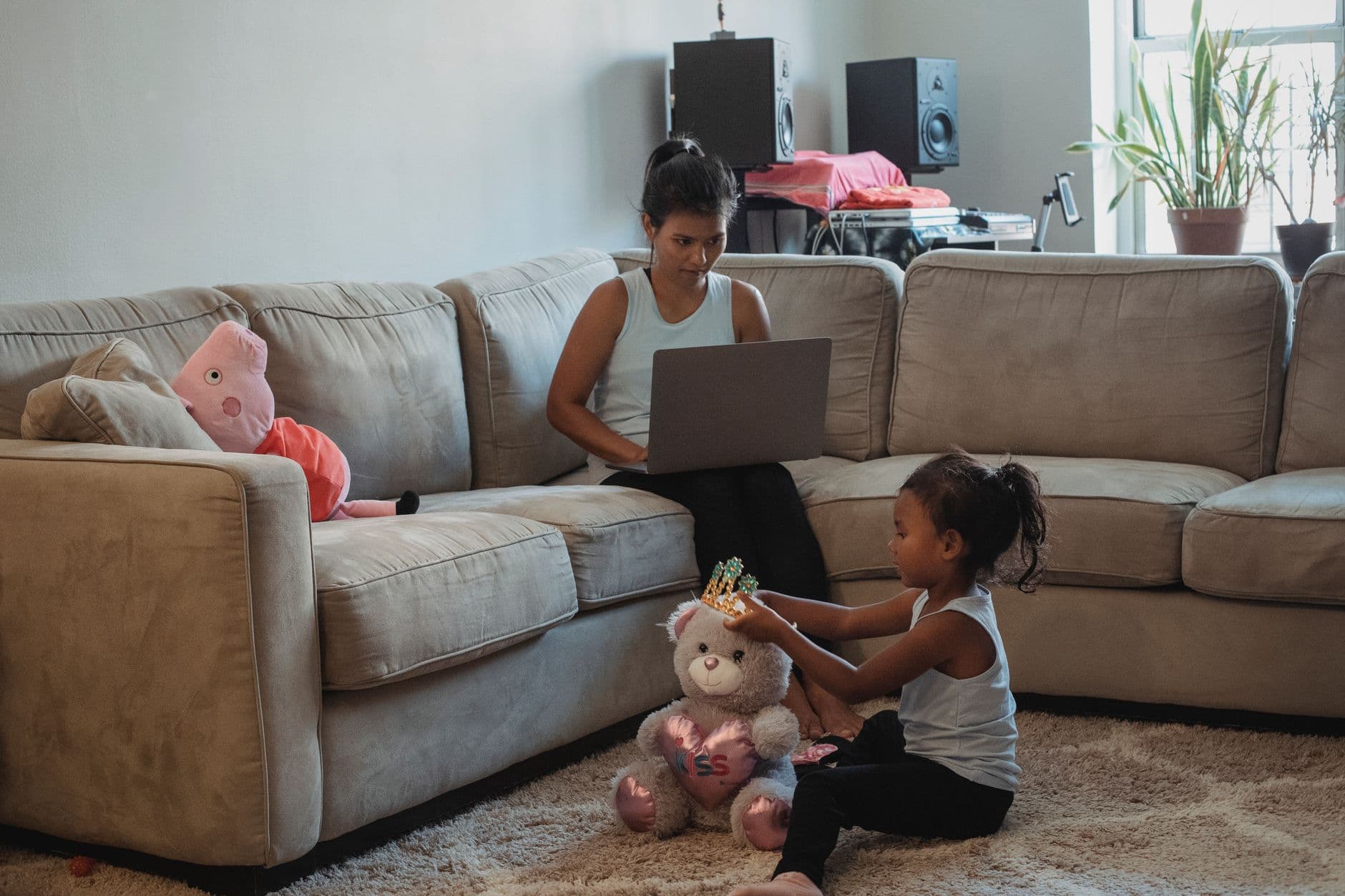 A mother working on a computer on the couch while her daughter plays with toys