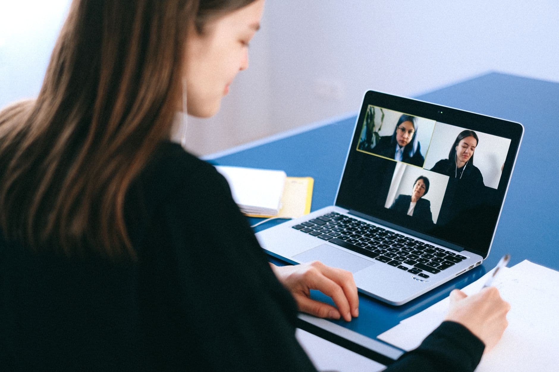 A woman on a video call at her laptop taking notes