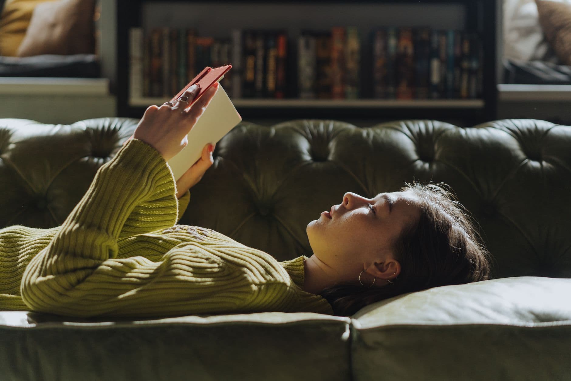 A young woman lying on a sofa reading a book