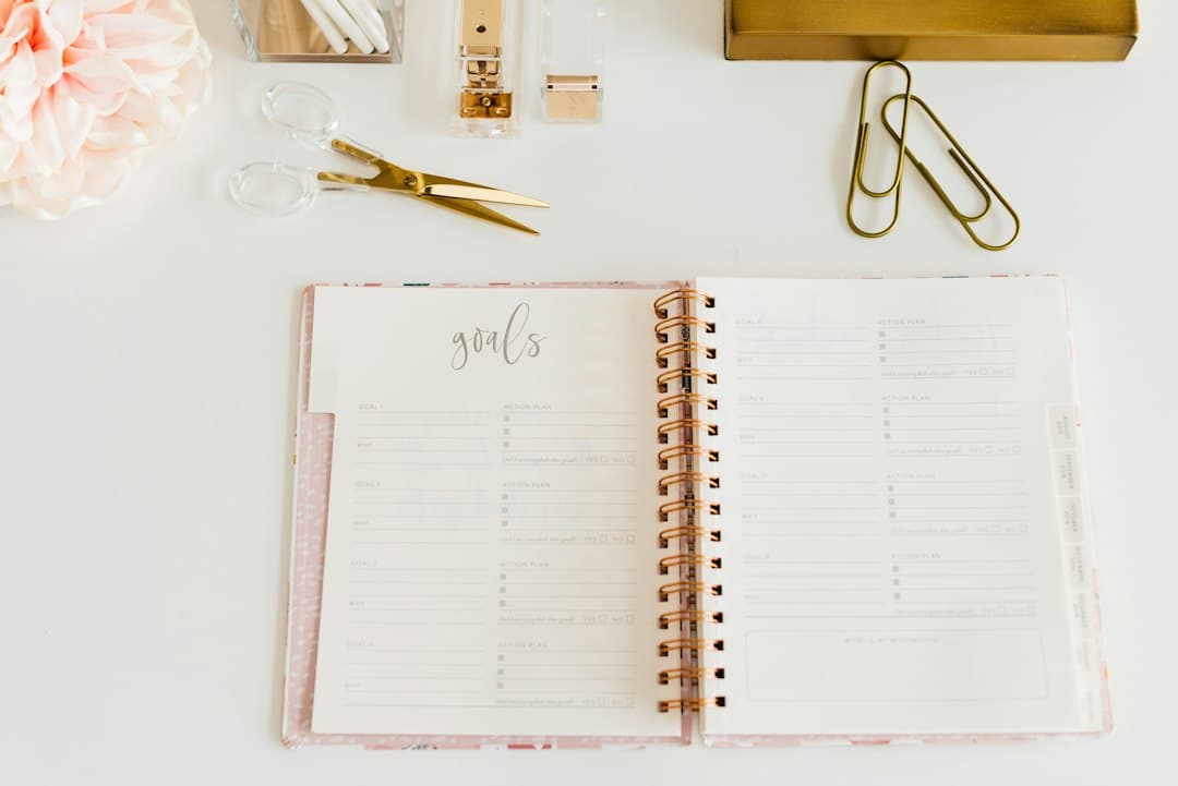An open spiral notebook with scissors and paper clips on a desk