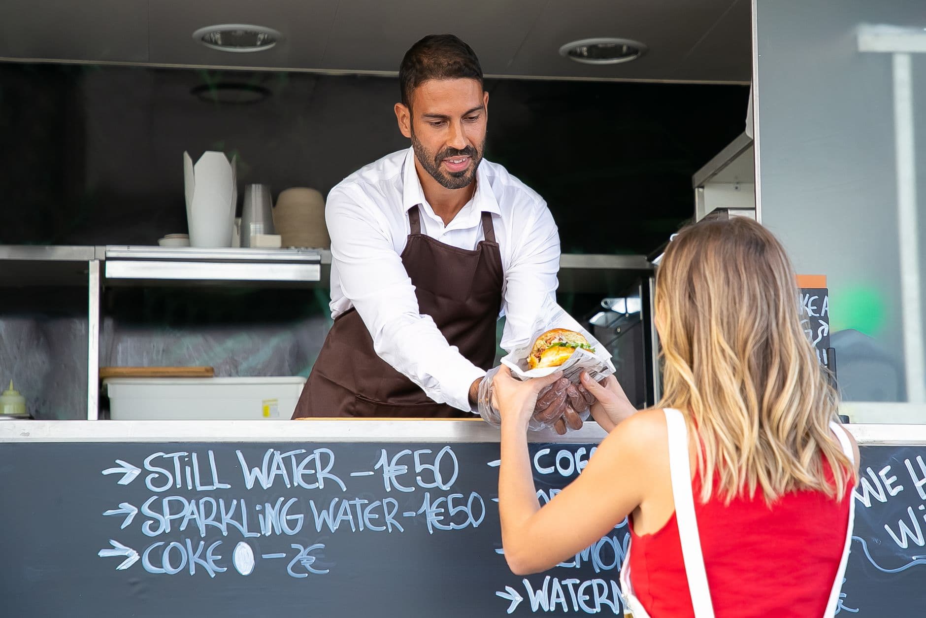 A food truck cook handing a burger to a customer
