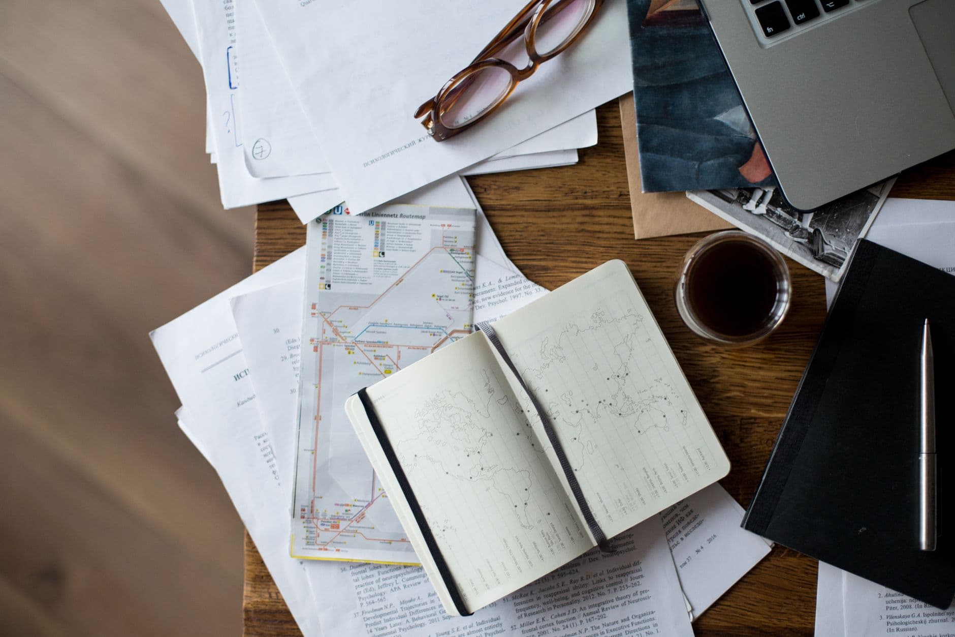 A workspace with coffee, maps and a laptop on a wooden desk