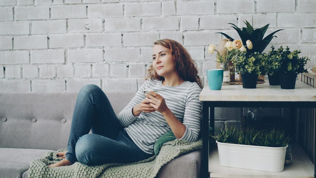 A woman relaxing on a sofa with her phone and a coffee