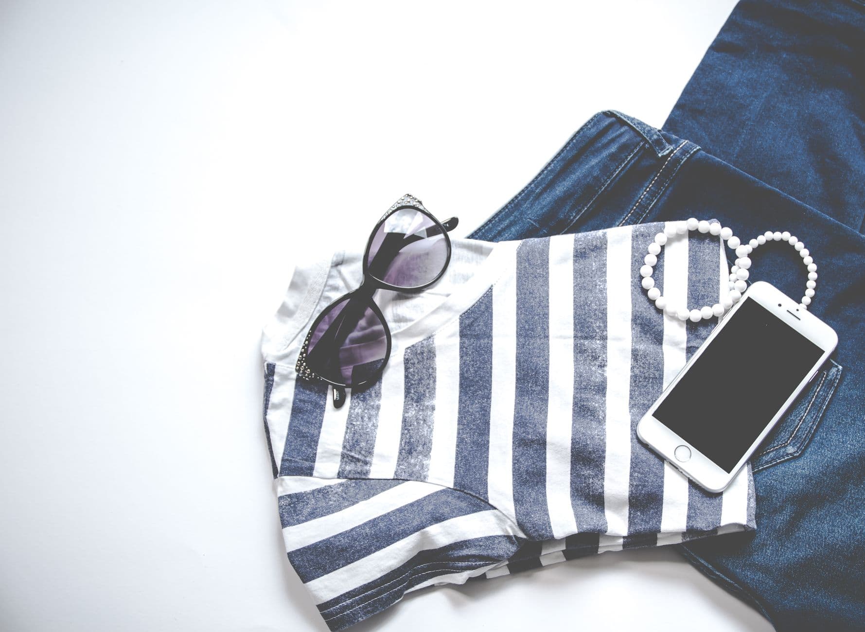 A flat lay of a striped top, jeans, sunglasses and a smartphone