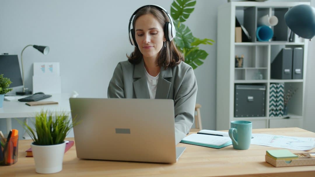 A woman wearing a headset while working on a laptop at her desk